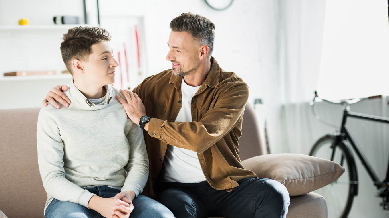 father hugging teen son on sofa at home