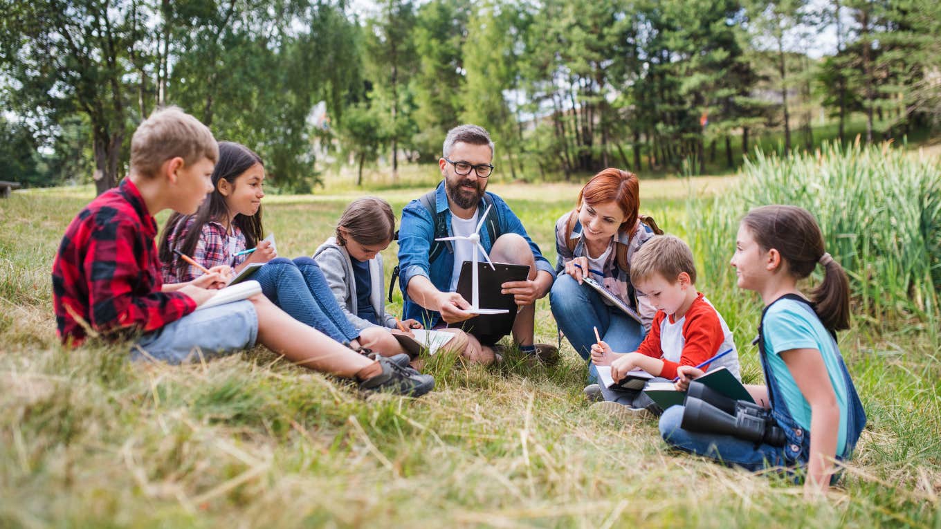 Group of school children with teacher and windmill model on field trip in nature.