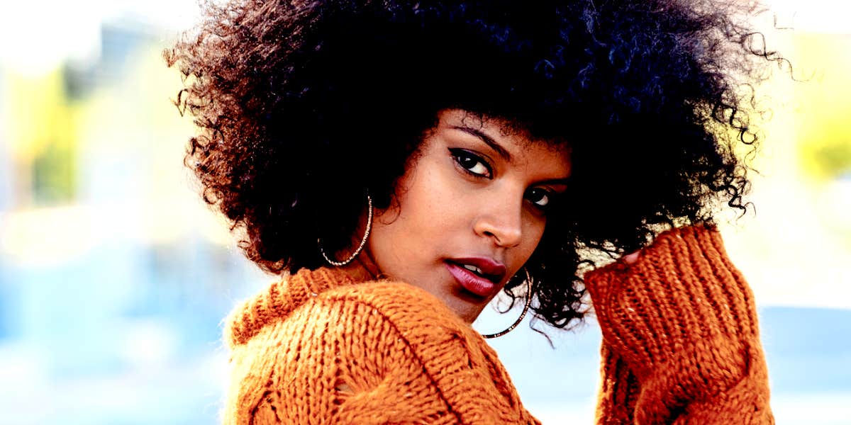 young Black woman with natural hair looks at camera in orange sweater