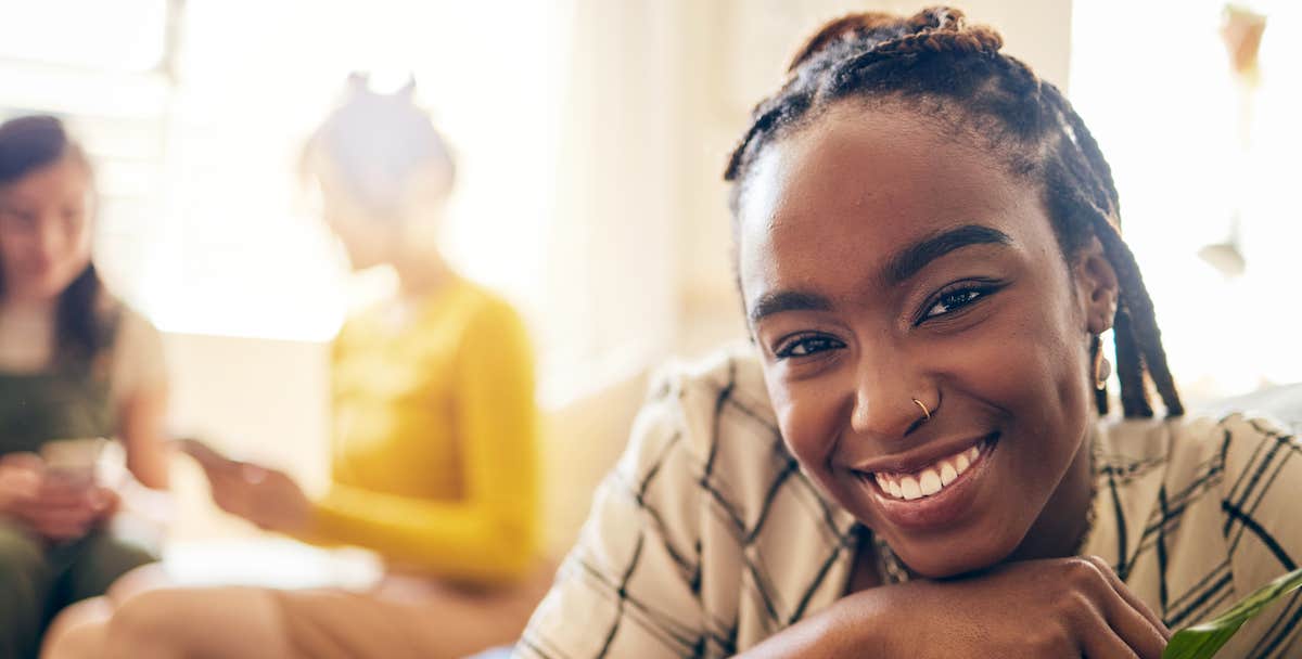 happy woman smiles and leans in to the camera while friends discuss plans in the wash of morning light that sweeps the background