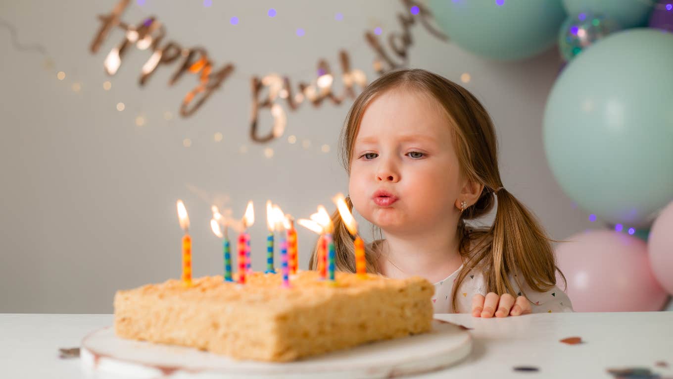 little girl blowing out candles on birthday cake in front of decorations