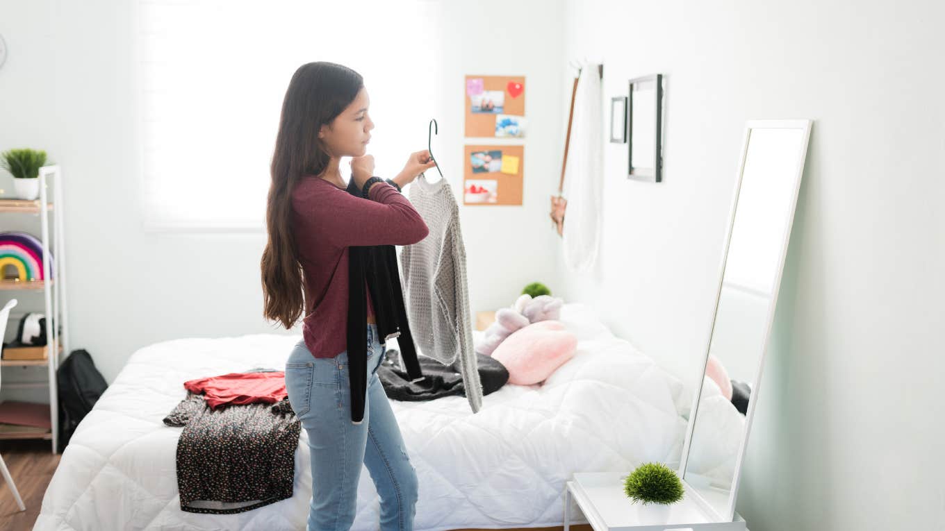 teenage girl standing in her bedroom and trying different outfits in front of the mirror.