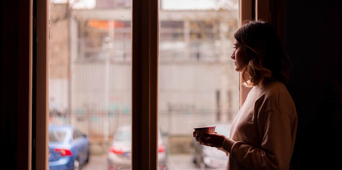 depressed girl standing near window in dark room