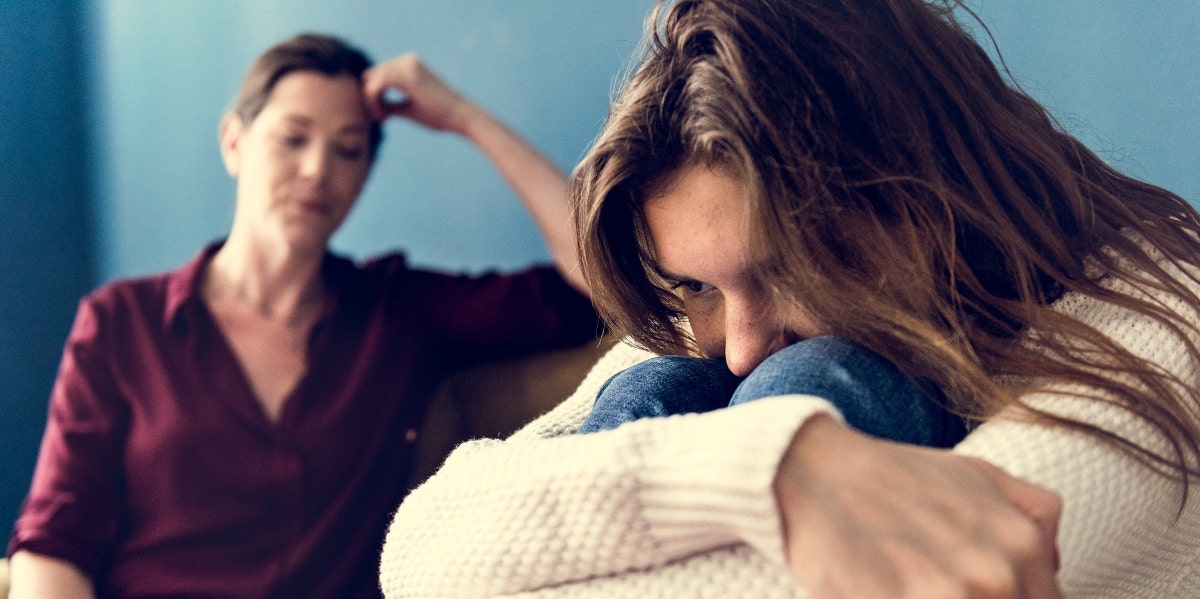 teen girl crying with mom behind her