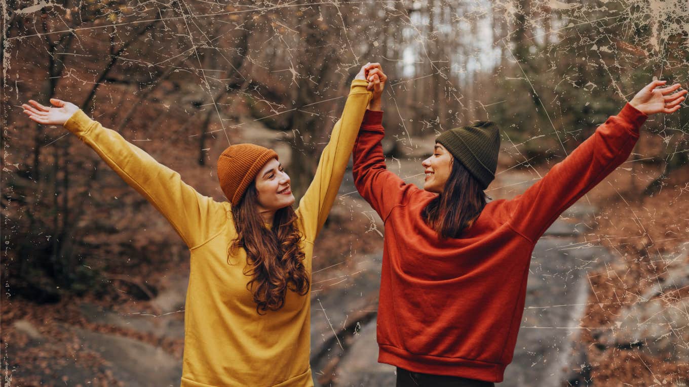 two friends with their arms up having fun outdoors
