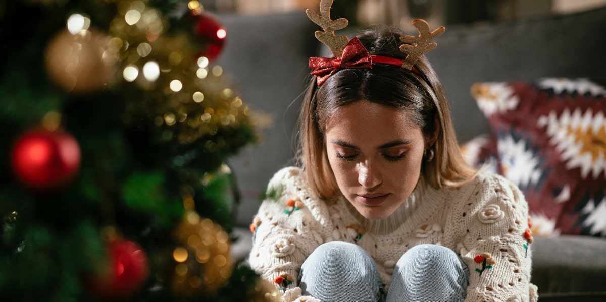surviving the holidays sad woman sitting in front of a Christmas tree