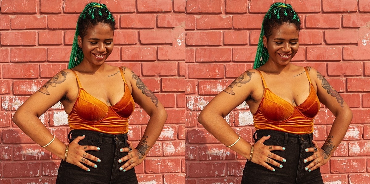 woman with low cut top green hair smiling against brick wall