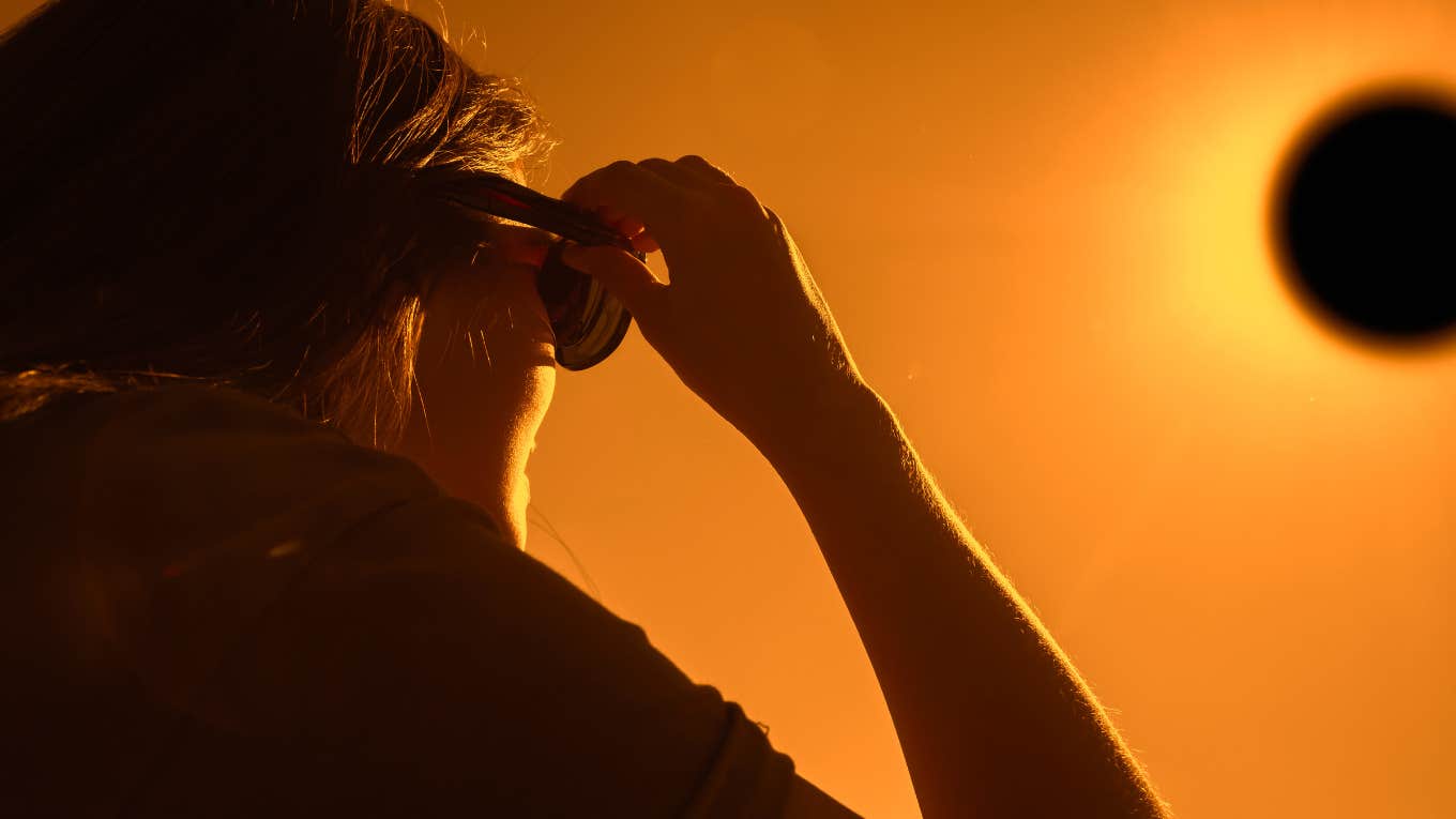 back view shot of woman looking at solar eclipse through three sunglasses