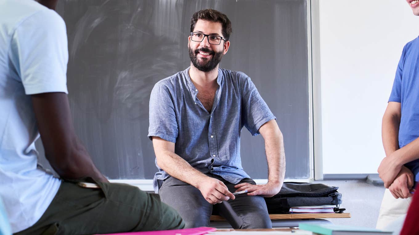 Male teacher sitting on a desk talking to students