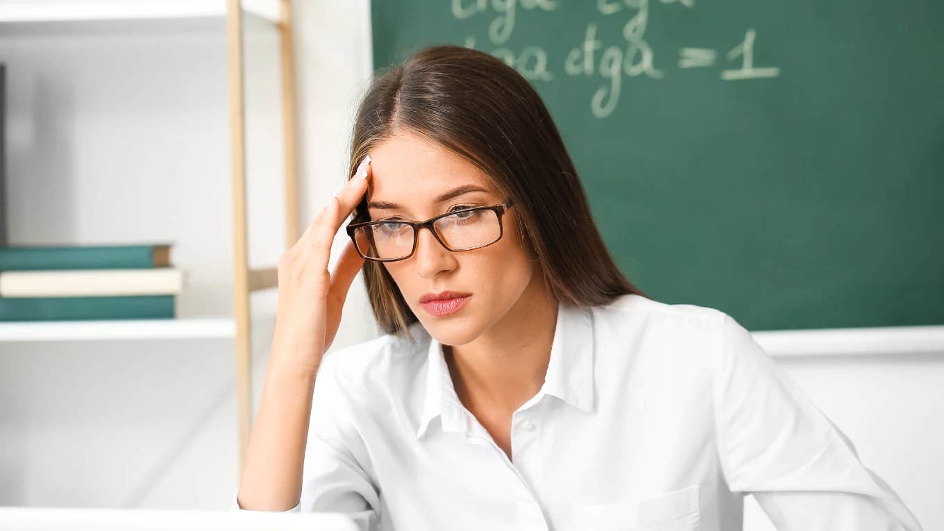 sad teacher sitting in front of chalkboard