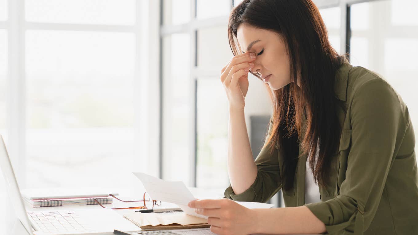 exhausted woman sitting at desk in front of laptop with her hands on her face