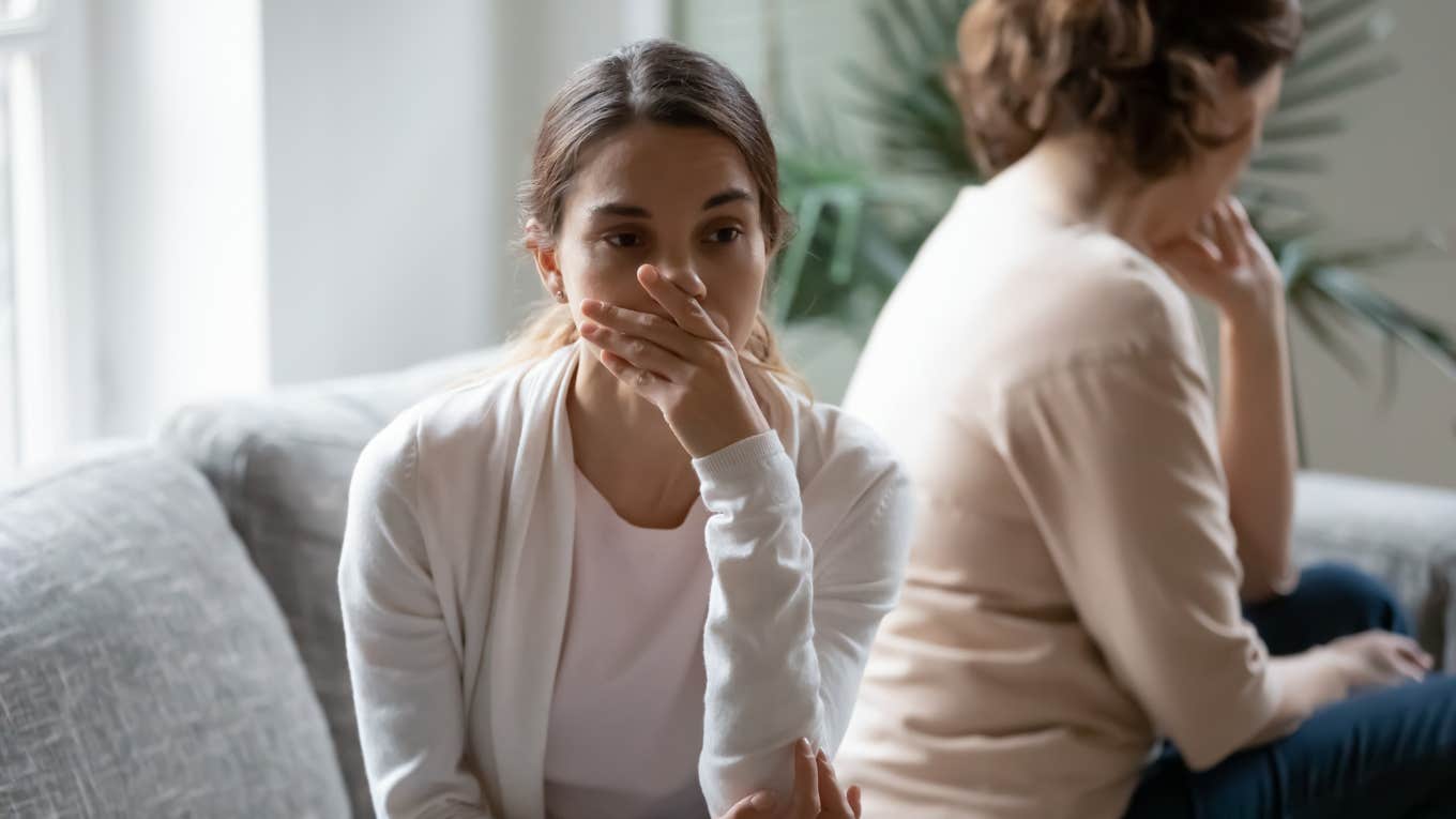 close up shot of upset daughter sitting with back turned to angry mother on couch