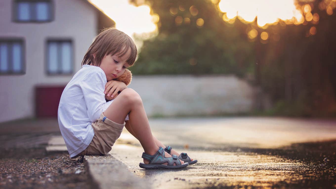 little boy sitting on street curb holding stuffed animal