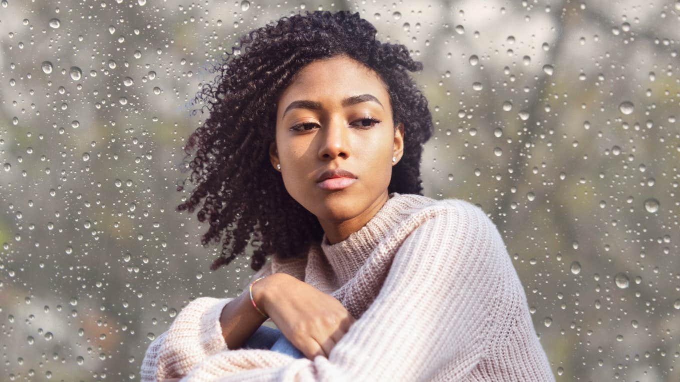 The Mental Trick That Can Help People Heal From Parental Abandonment Or Neglect Woman looking solemn next to a rainy window.
