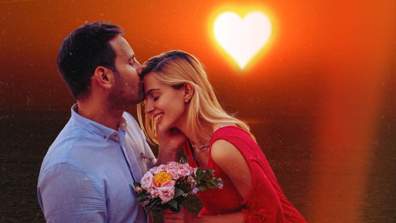 3 Tiny Secrets To Getting The Love You Want, According To Relationship Experts Man kissing woman on forehead in front of sunset
