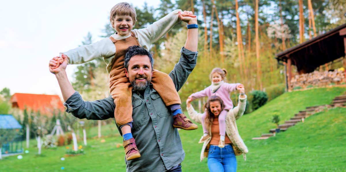 dad carrying child on shoulders with mom and sister in background