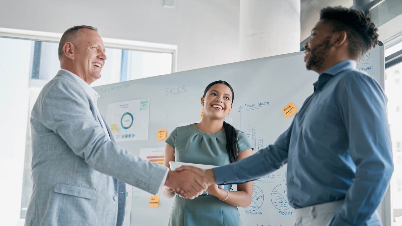 boss smiling while shaking employee's hand in meeting room