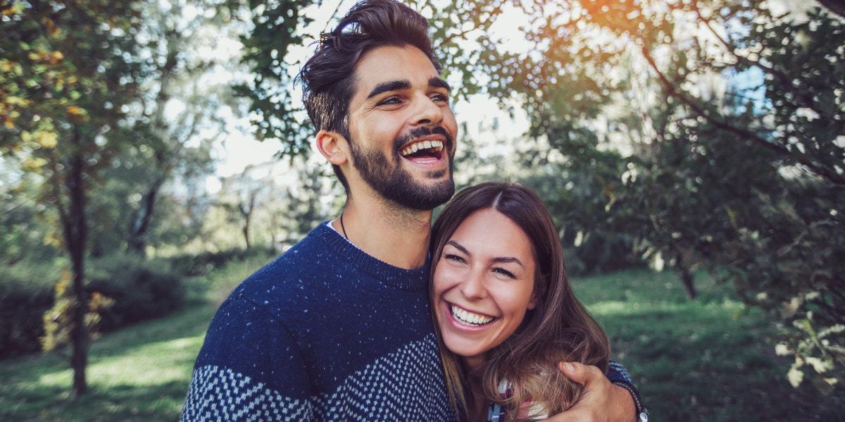 man and woman hugging with trees behind them