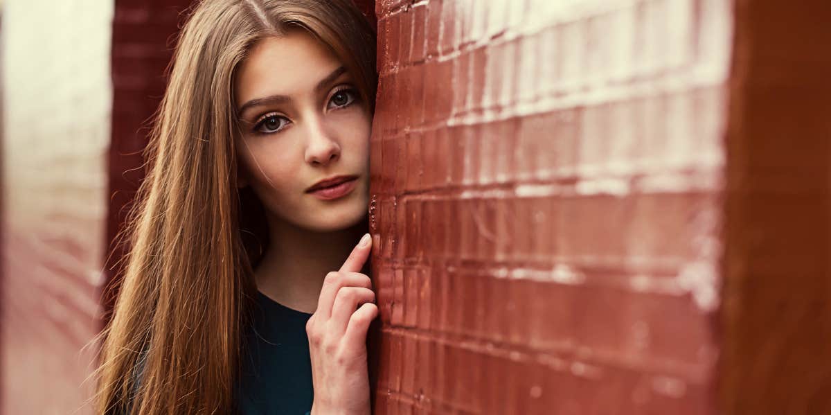 woman looking out from behind a brick wall