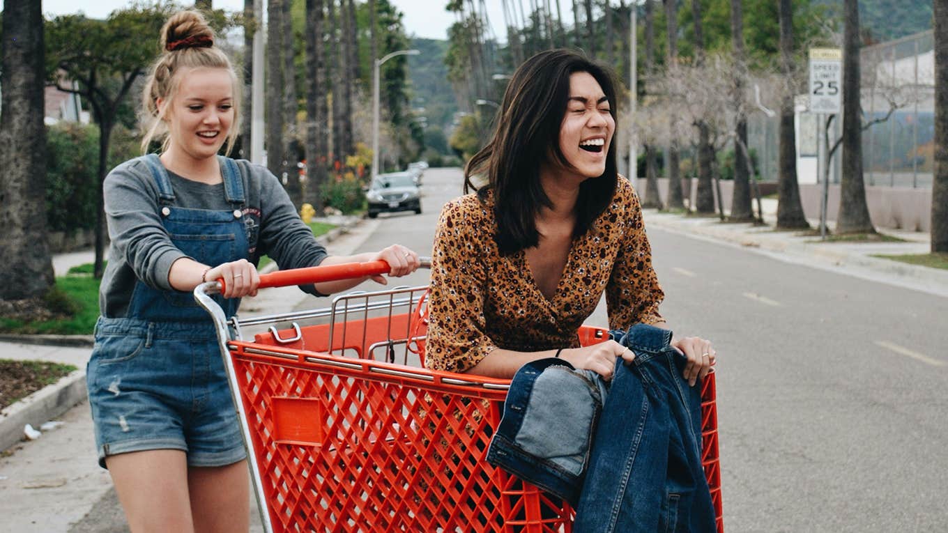 two women laughing in a shopping cart on the street