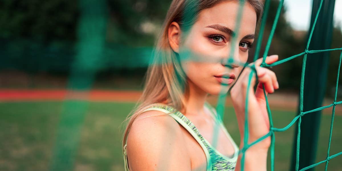 4 Harsh Things Men Will Never Experience (But Women Regularly Do) woman peering through soccer net