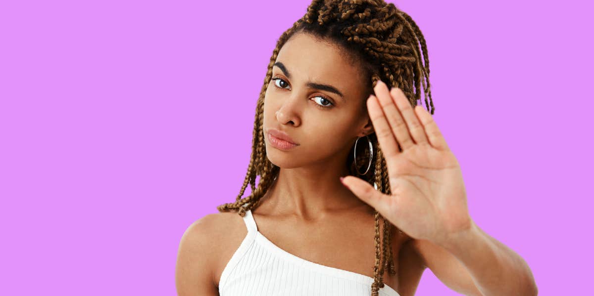 beautiful woman in front of purple background holding up her hand to say no