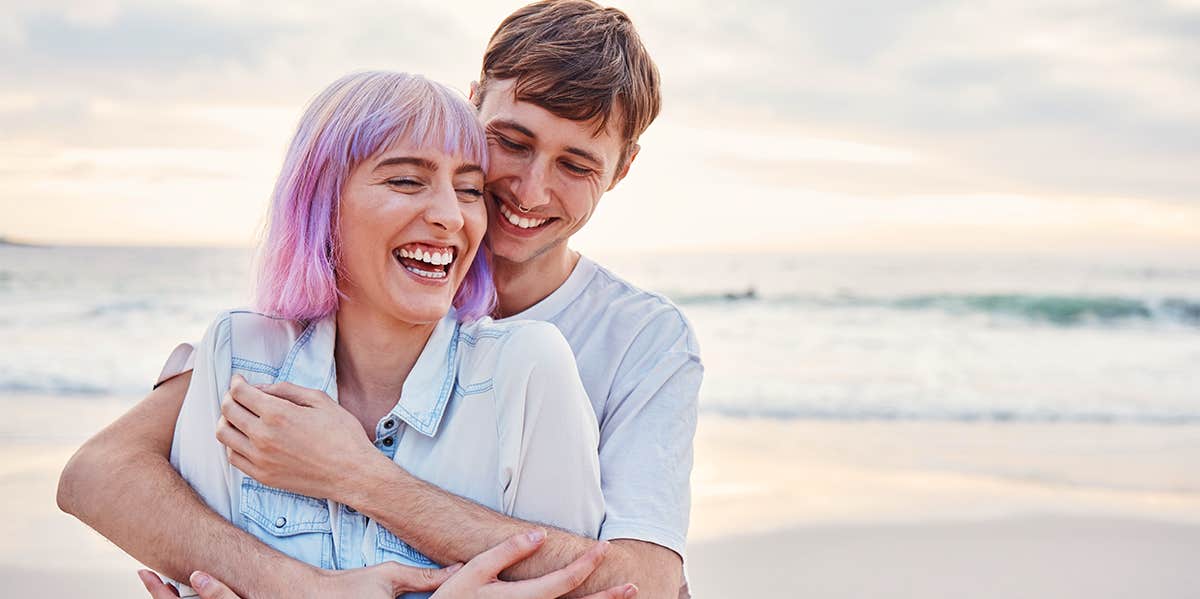 guy hugging girl from behind on beach