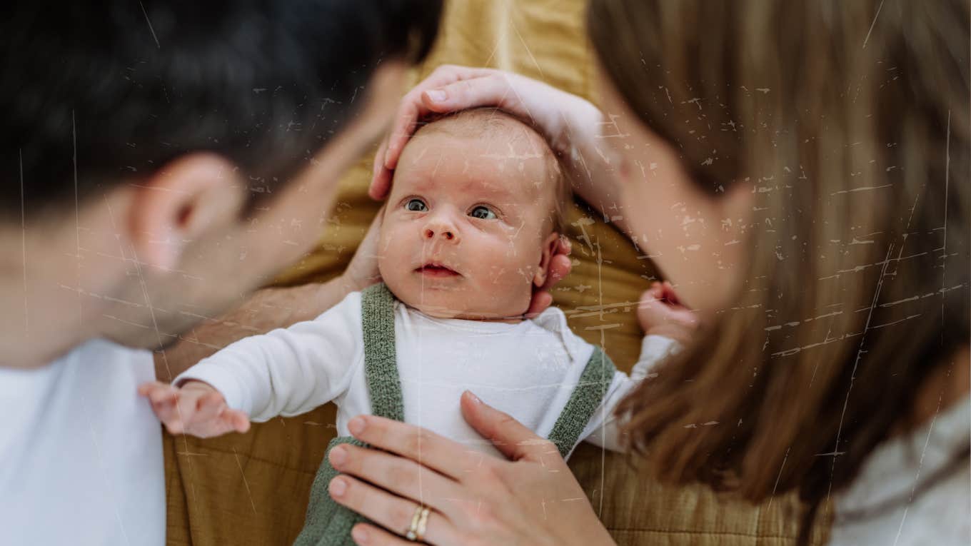 baby looking towards father while both parents hold her