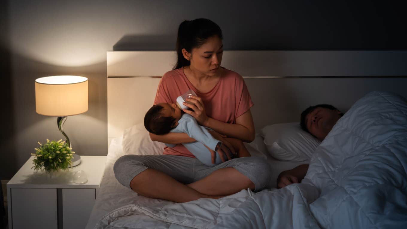 mother exhausted bottle feeding newborn while father sleeps