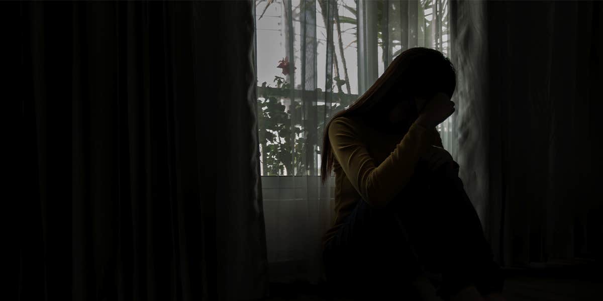 sad woman sitting by window in the dark