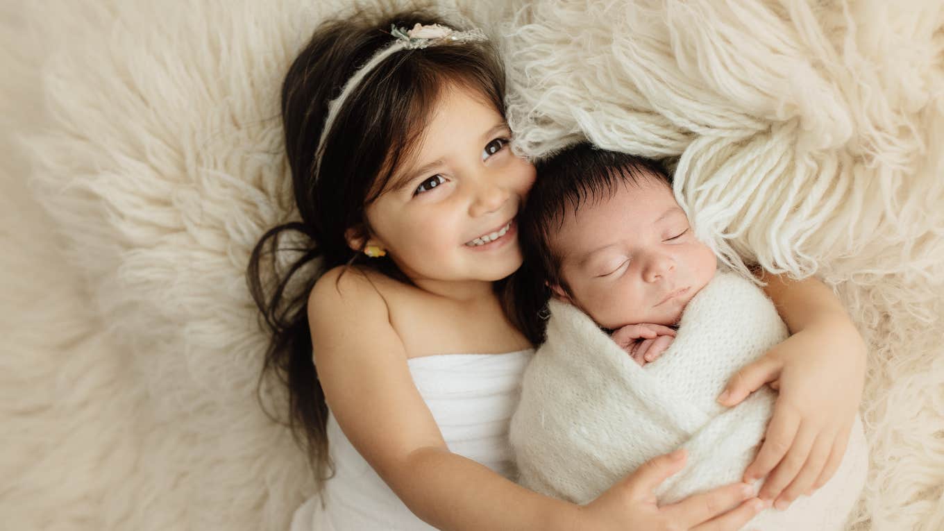 toddler sister hugging infant brother