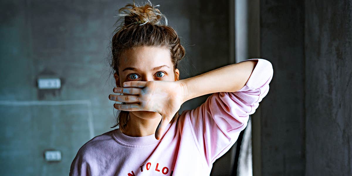 woman in topknot with big blue eyes and a pink hoodie covers her face