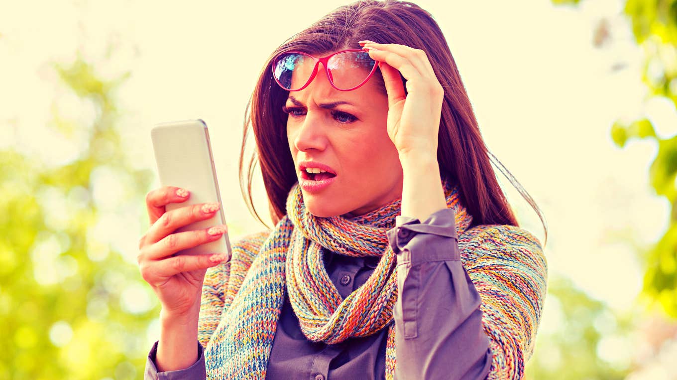 Annoyed upset woman in glasses looking at her smart phone with frustration