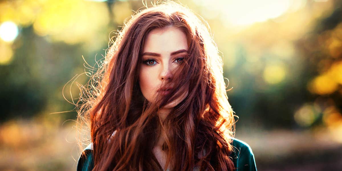 serious redhead woman in the forest, hair blowing across her face