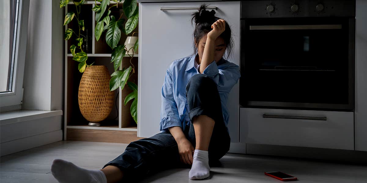 Woman sitting on kitchen floor with her face covered by her arm