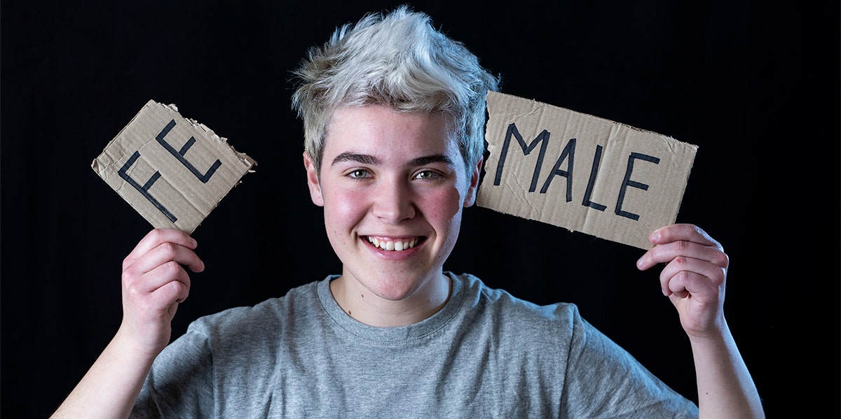 non-binary person holding up a female sign broken in half