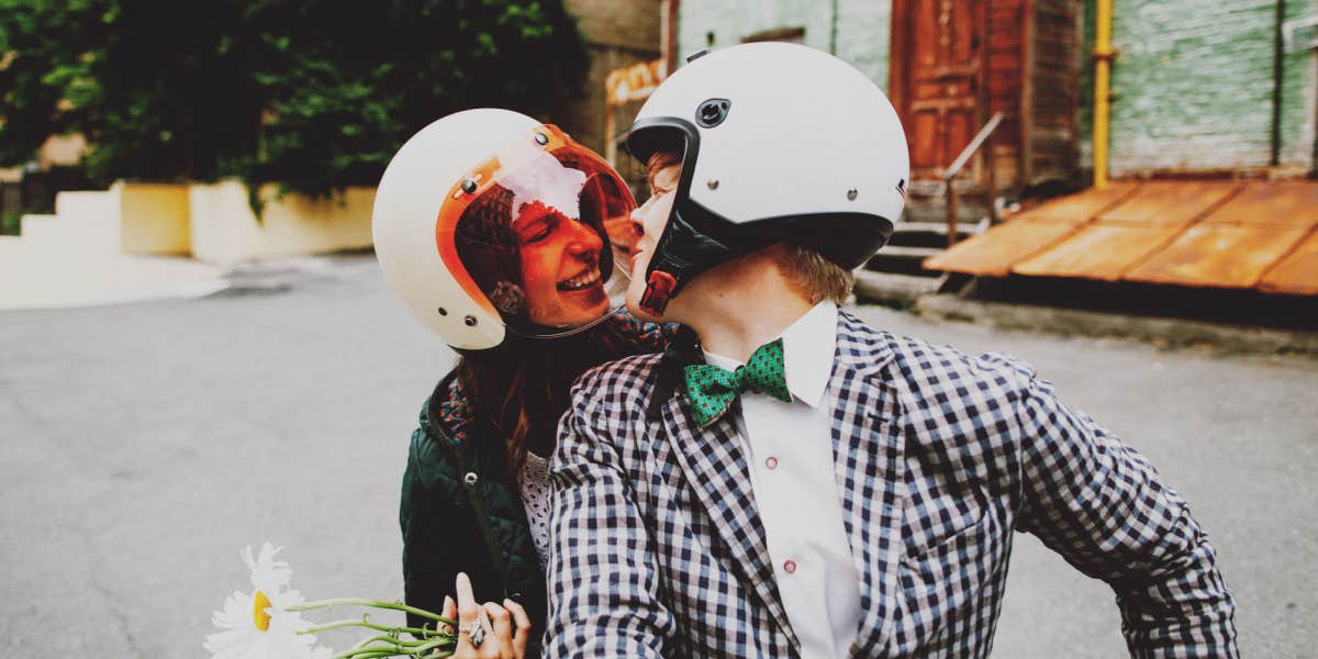 Couple on scooter in white helmets, kissing and smiling