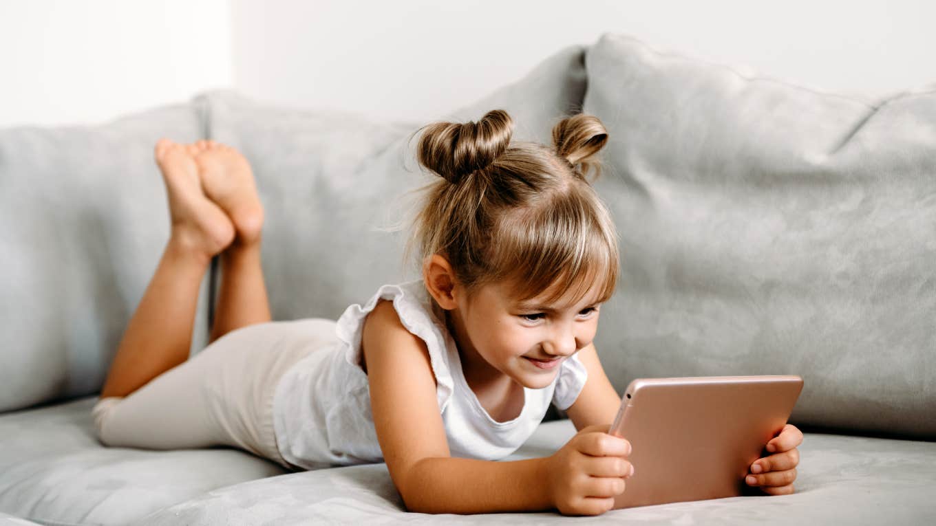 toddler girl playing on tablet while laying on couch