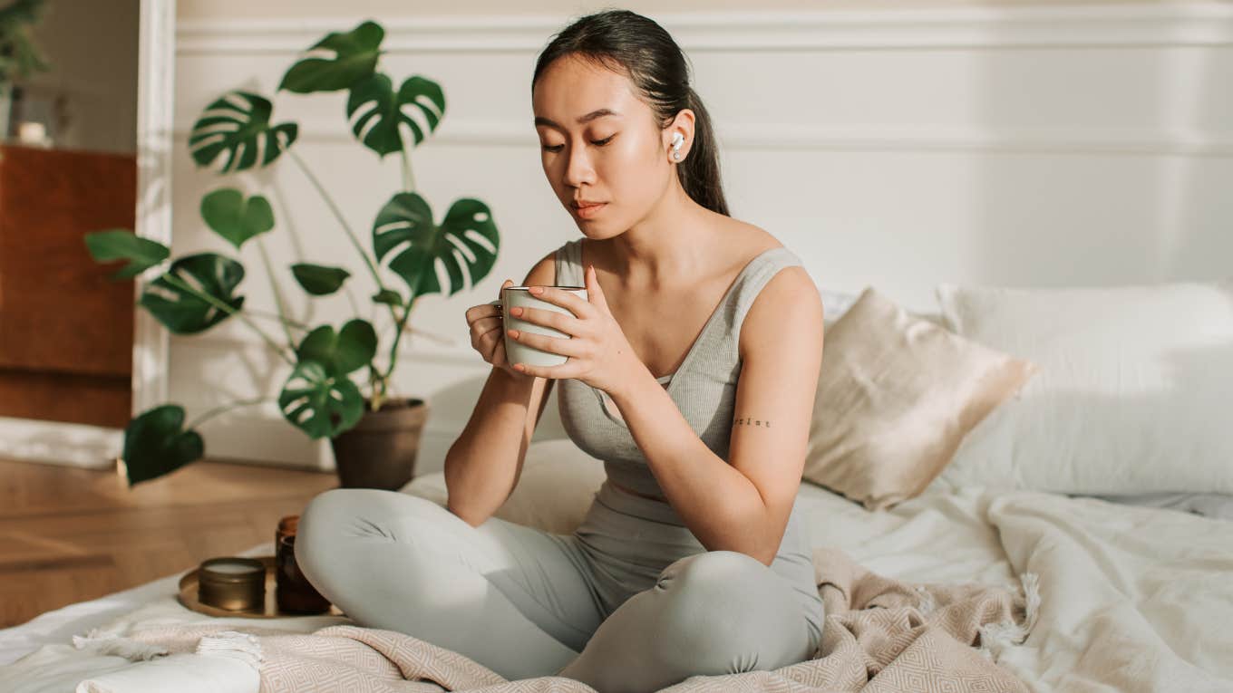 Woman sitting on her bed with a cup of coffee. 