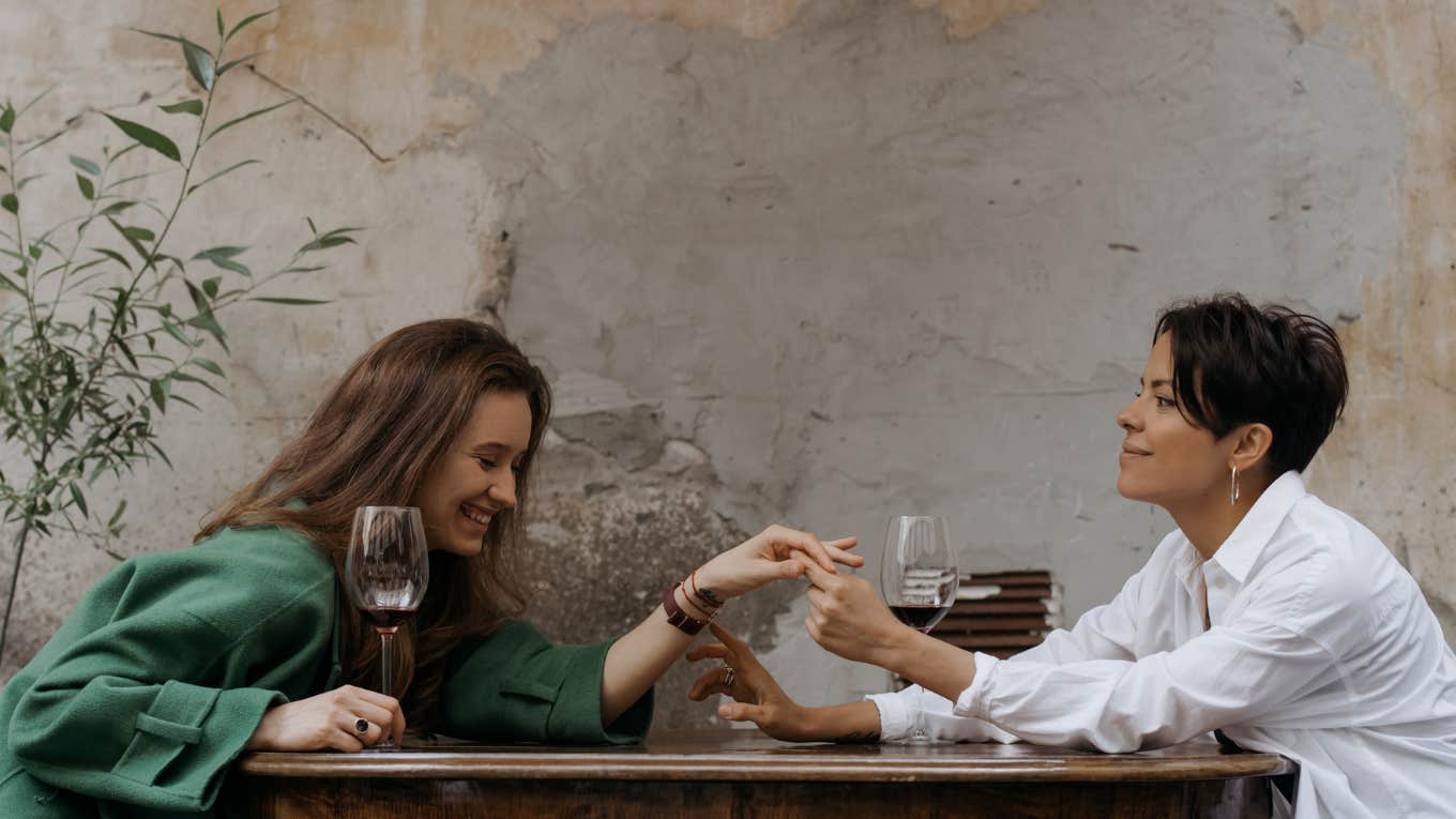 two women drinking wine holding hands 