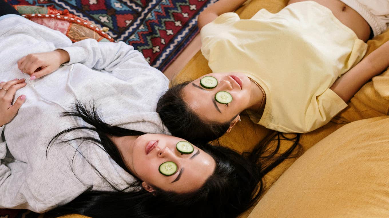 two people laying side by side with cucumbers on their eyes