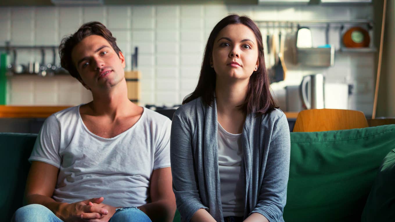 Lazy millennial couple getting bored at home sitting on sofa