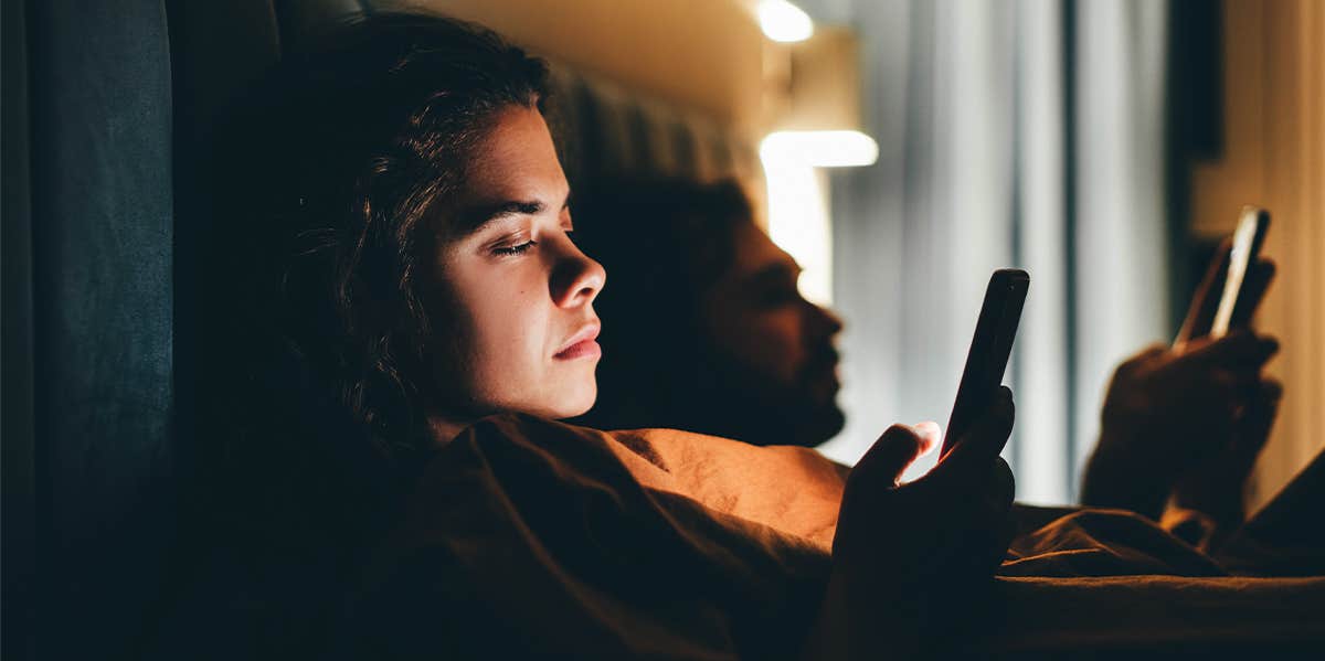 couple laying in bed looking at phones