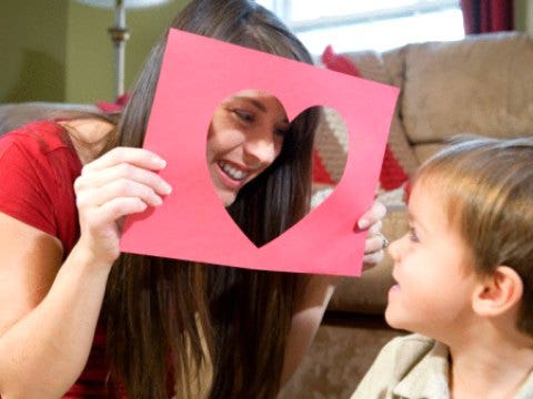 young woman peeking throught heart-shaped cutout at little boy