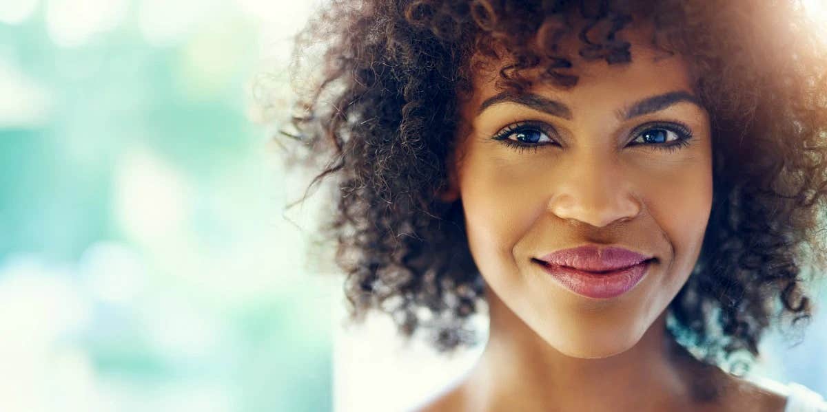 a content and happy woman looks at the camera, a slight burst of sunlight glows with her smile