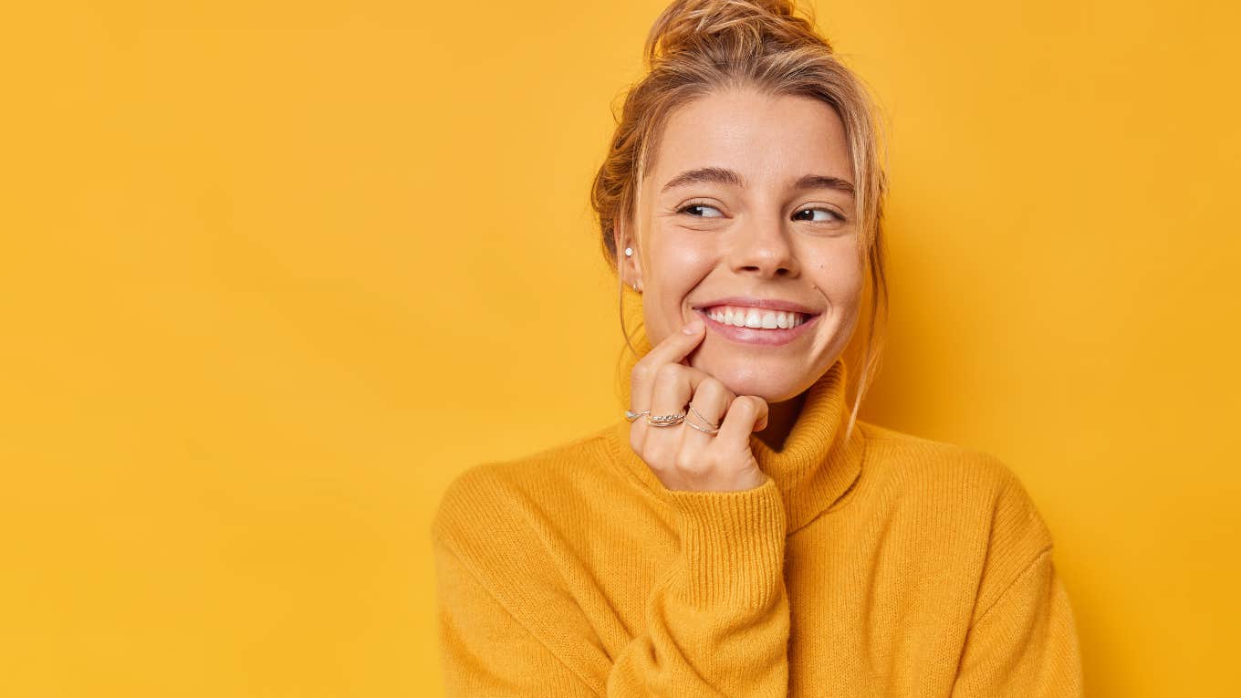 smiling woman pointing at her teeth in front of yellow background