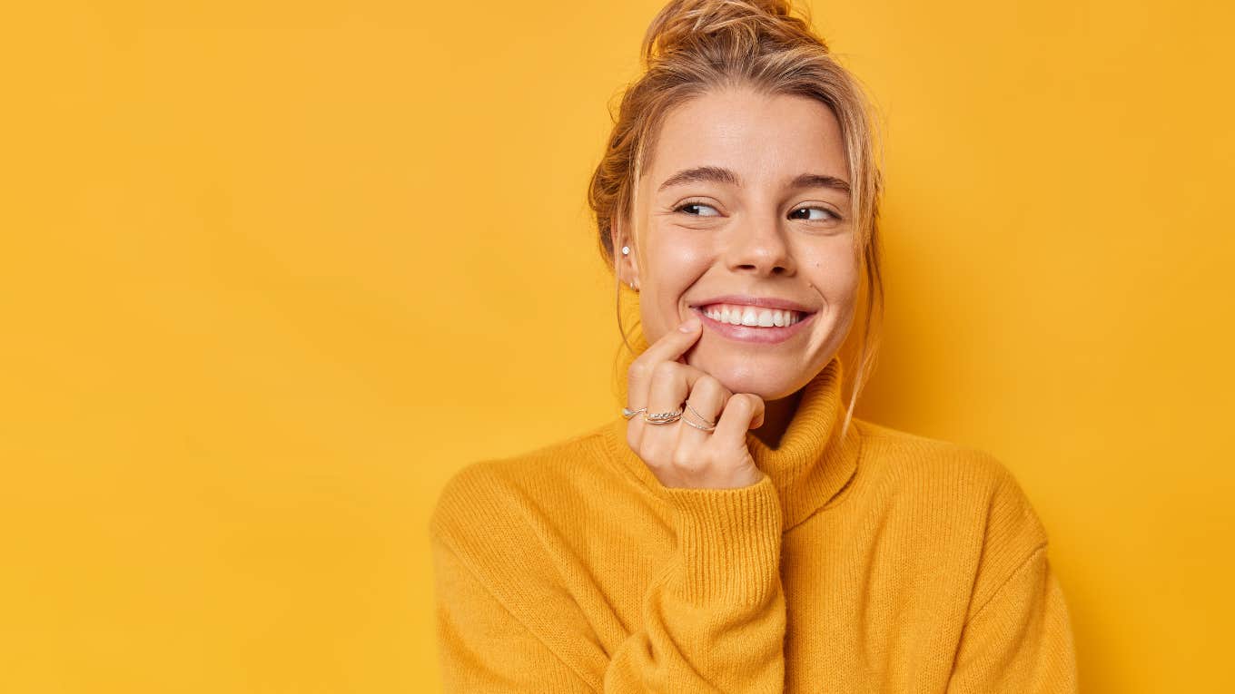 Main Causes Of Yellow Teeth And How To Reverse It smiling woman pointing at her teeth in front of yellow background