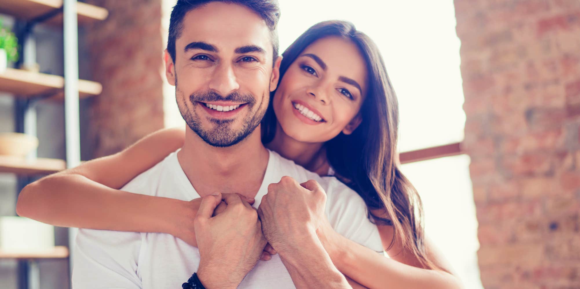 man smiling while girlfriend hugs him from behind