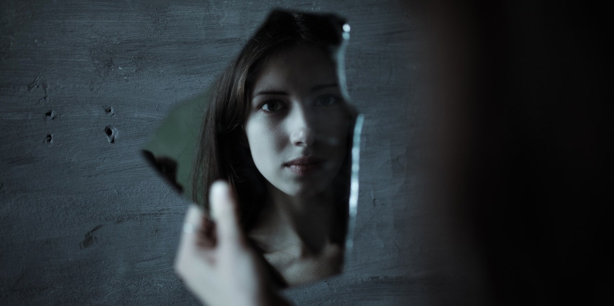 woman looking at broken mirror shard