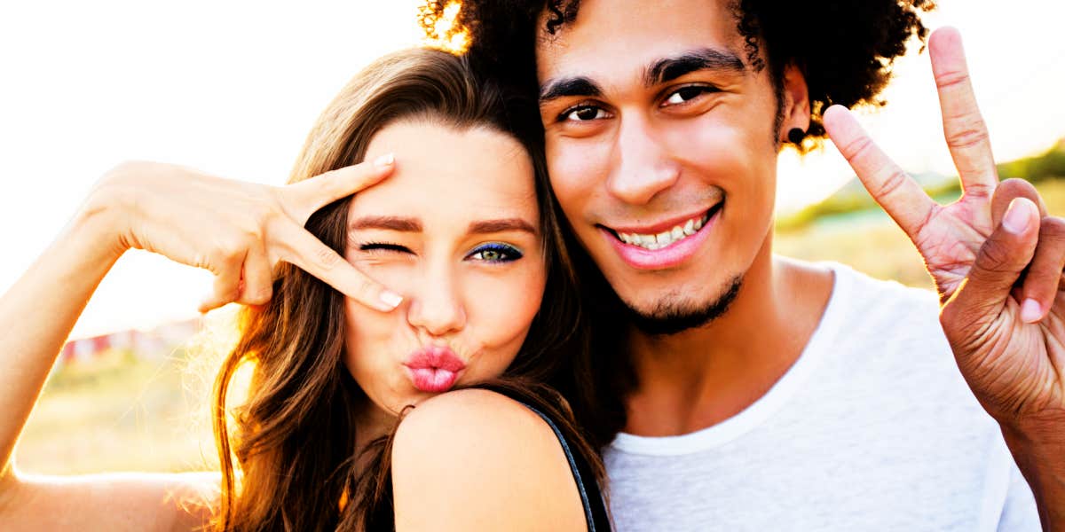 couple smiling in the sun, woman makes a peace sign